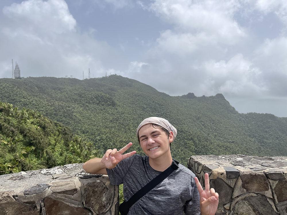 Caden Vitti poses in front of mountains at El Yunque, a national rainforest in Puerto Rico